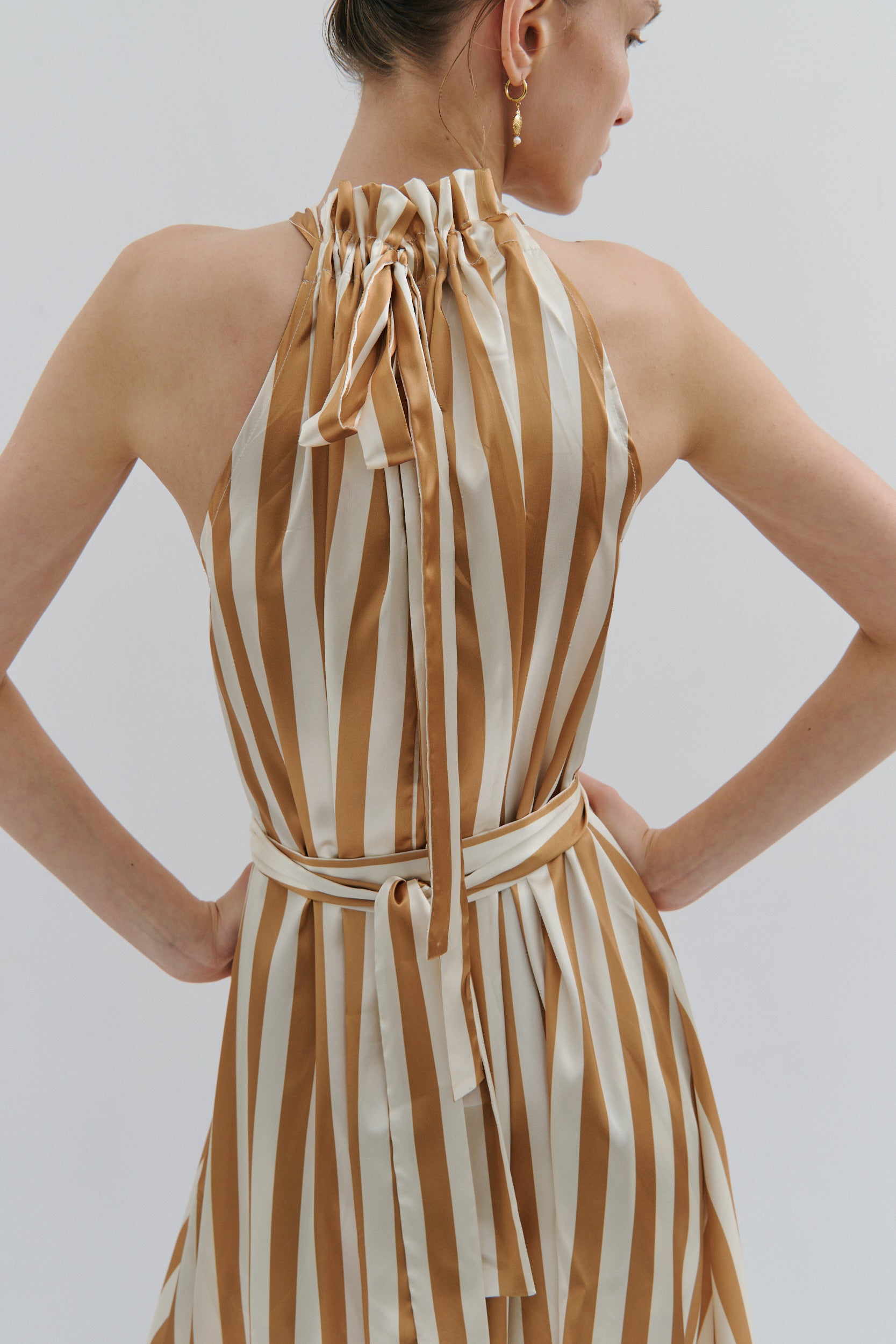 Woman wearing a gold and cream striped dress against a plain background