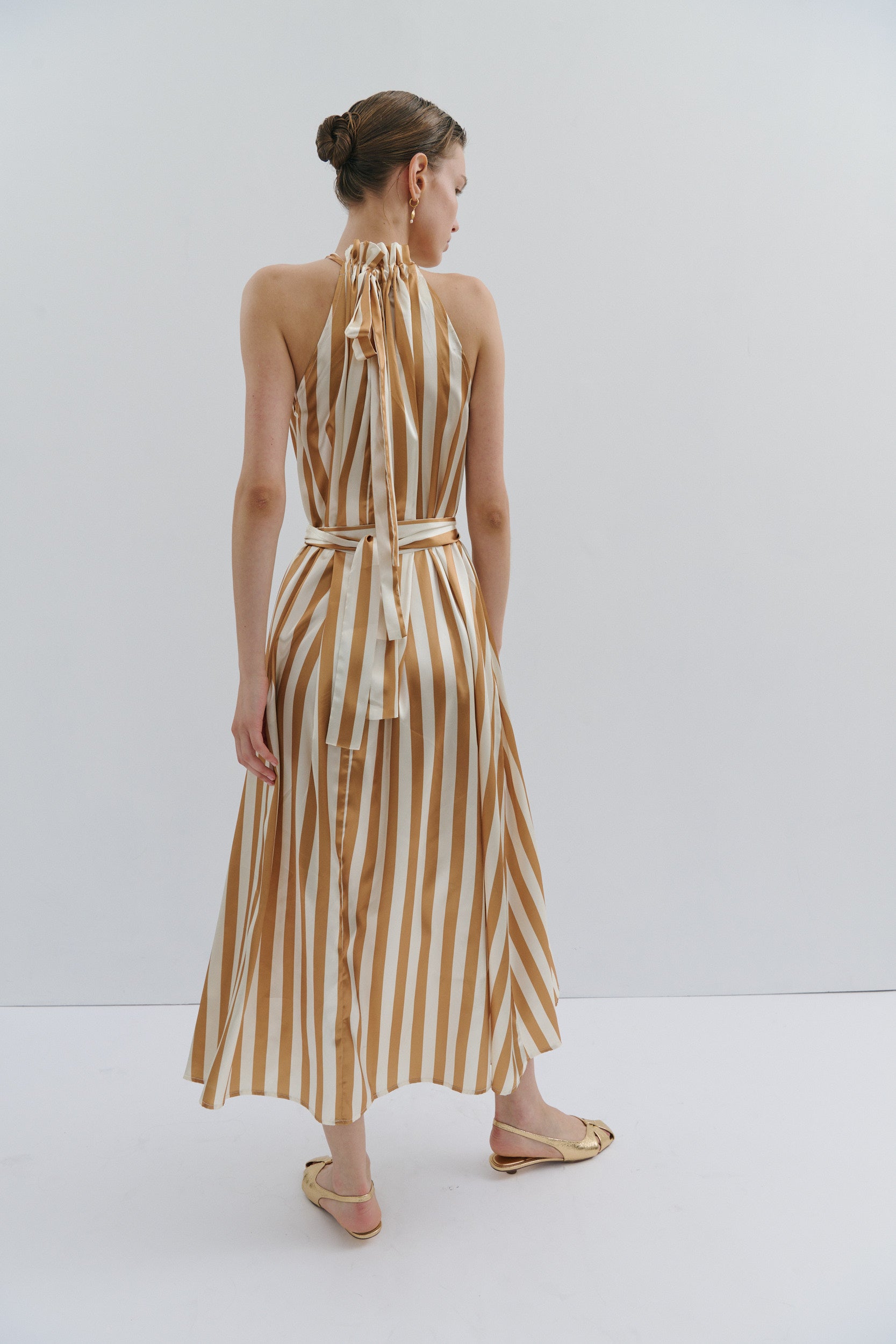 Woman wearing a gold and white striped dress against a white background