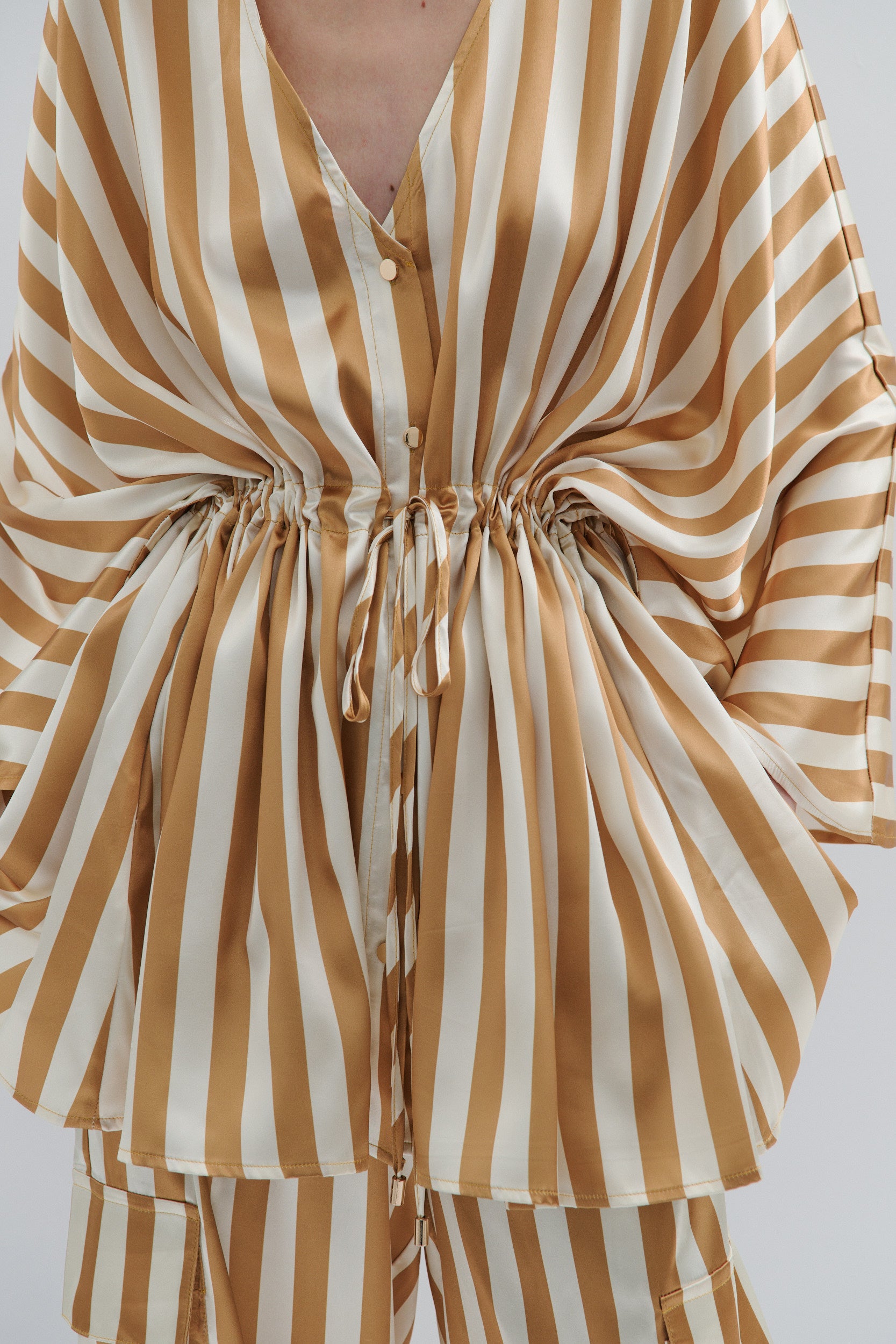 Striped kimono style jacket with gold buttons and drawstring waist in gold and cream vertical stripes on a plain background