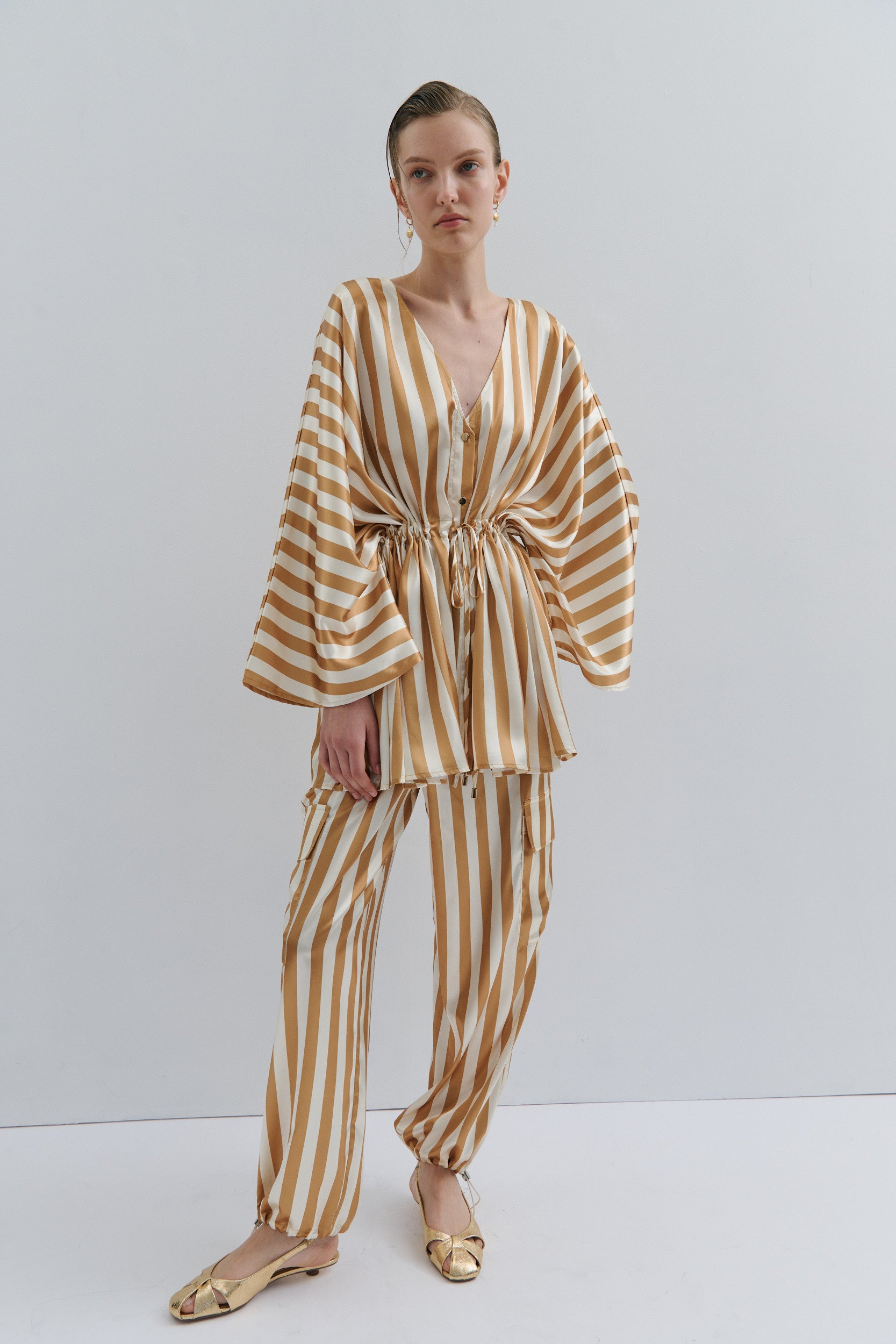 Woman wearing a gold and white striped jacket and pant on a white background