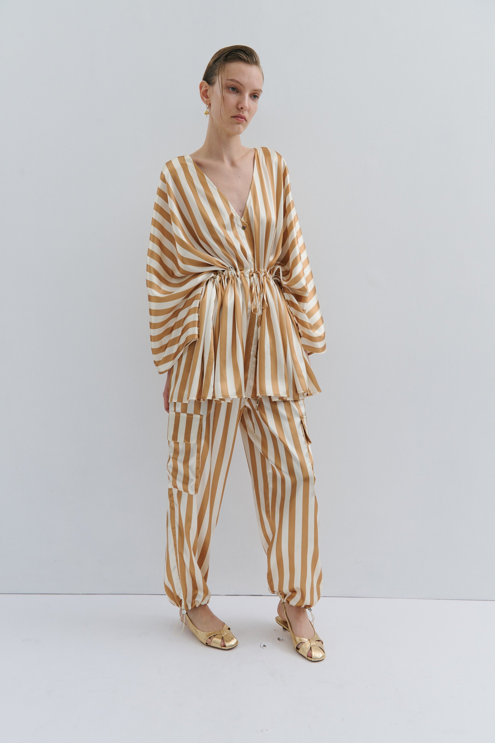Woman wearing a gold and white striped outfit against a white background