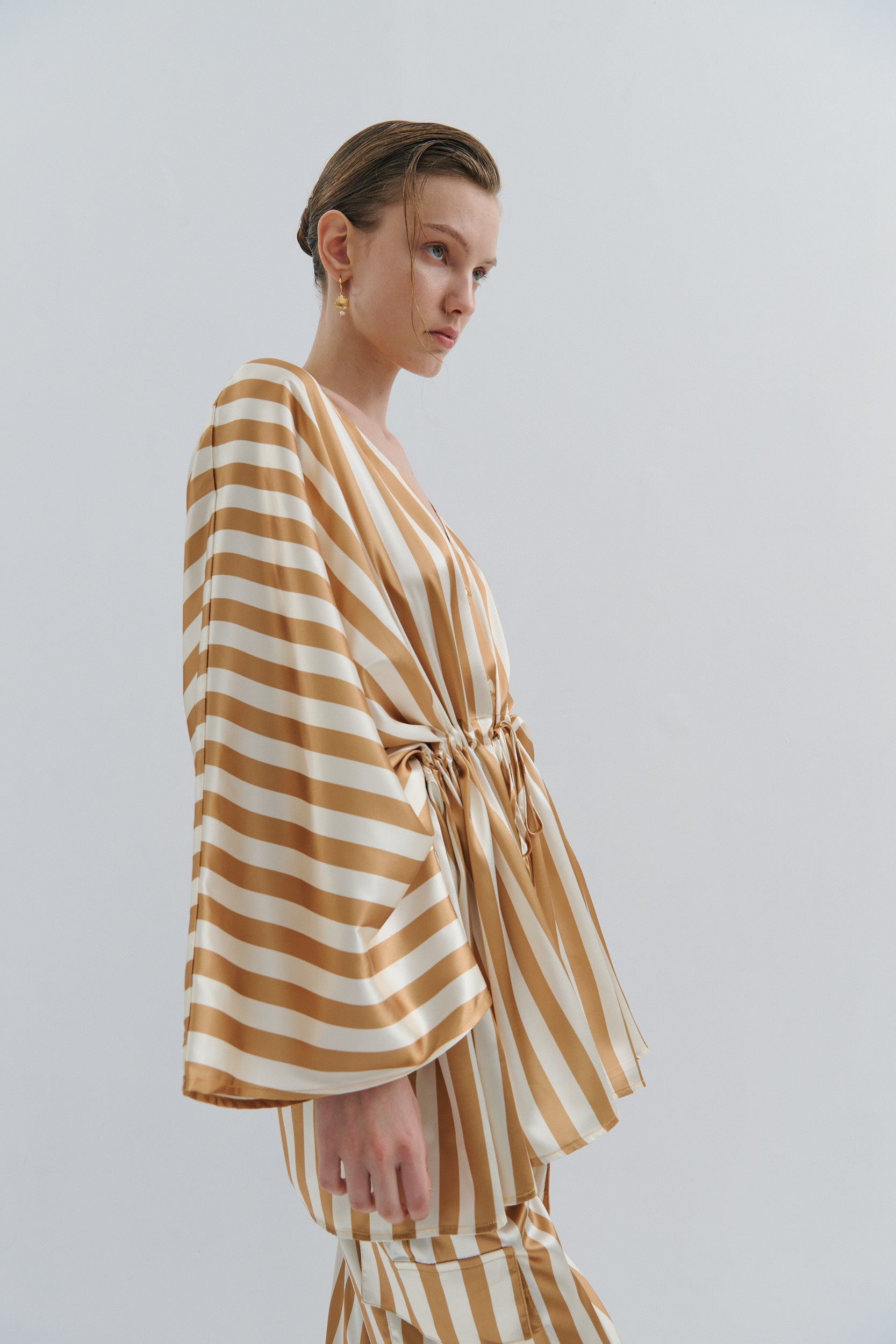 Woman wearing a gold and white striped jacket and cargo pant on a plain background