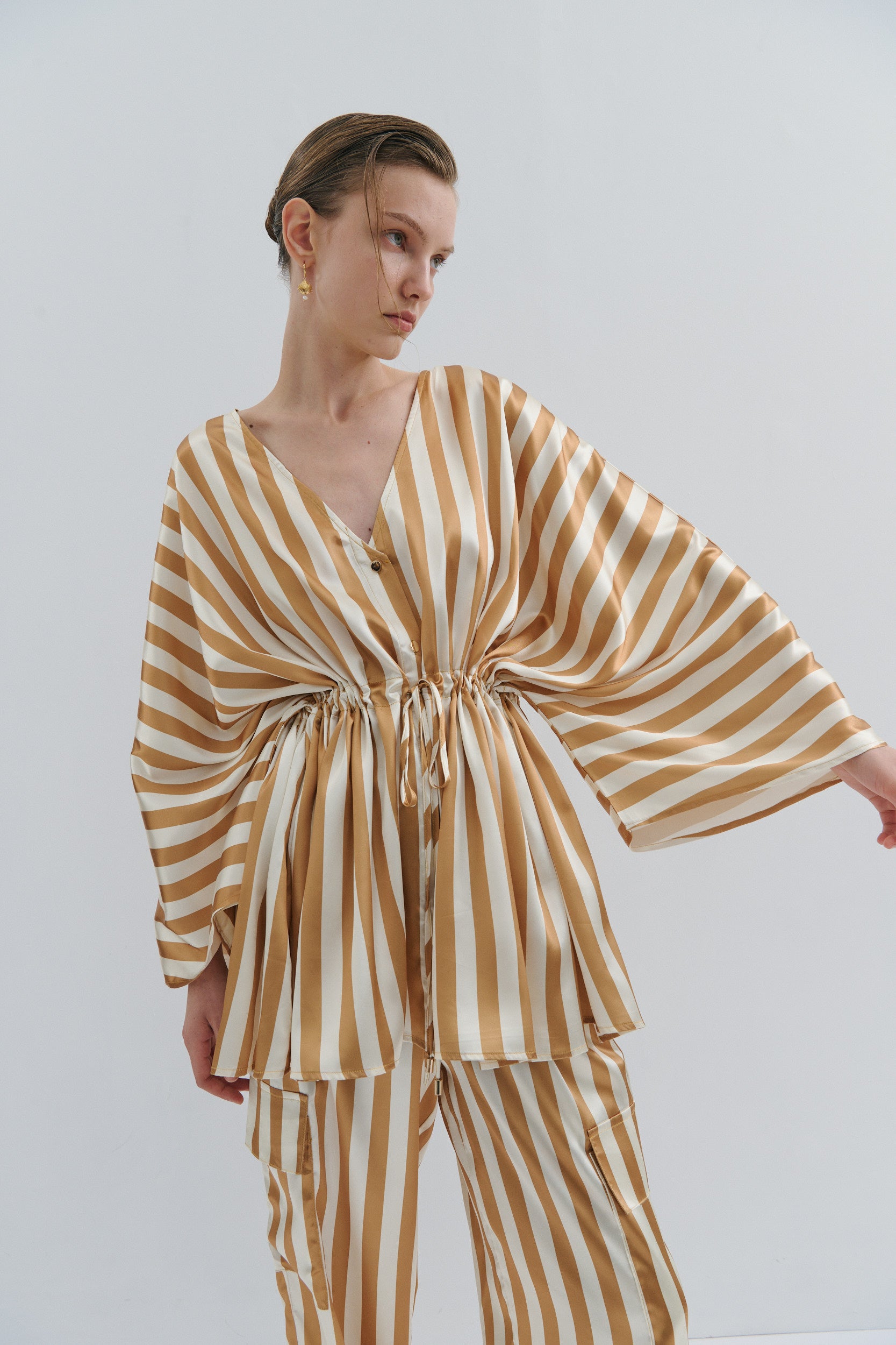 Woman wearing a gold and cream striped jacket with a plain background