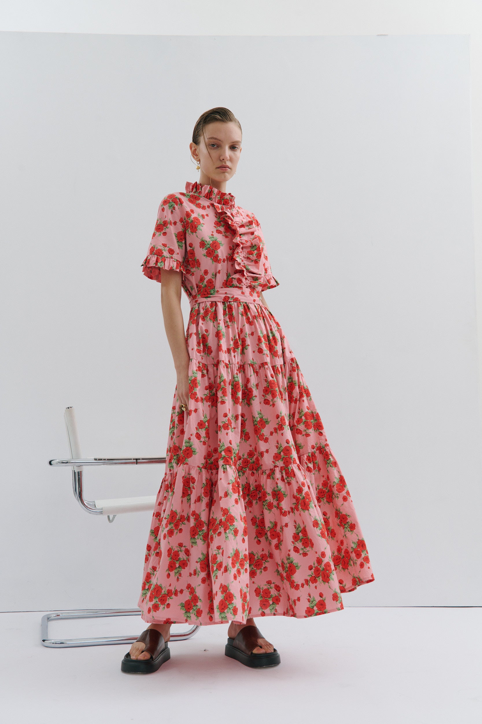Woman wearing a red floral dress sitting on a chair against a white background