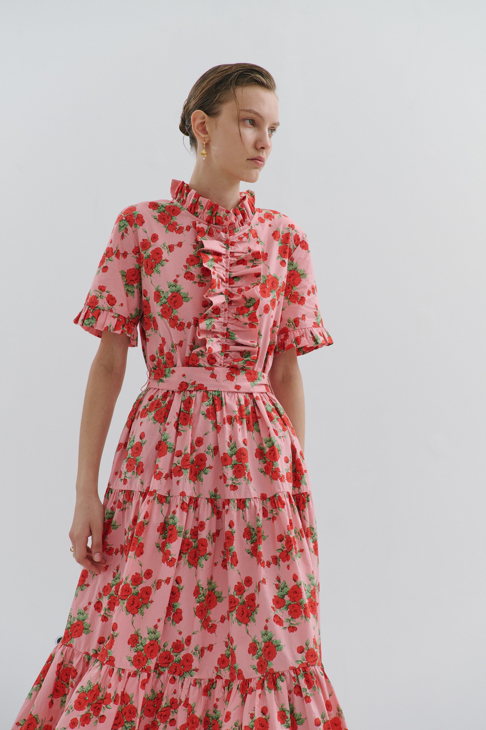 Woman wearing a pink dress with red floral pattern against a plain background