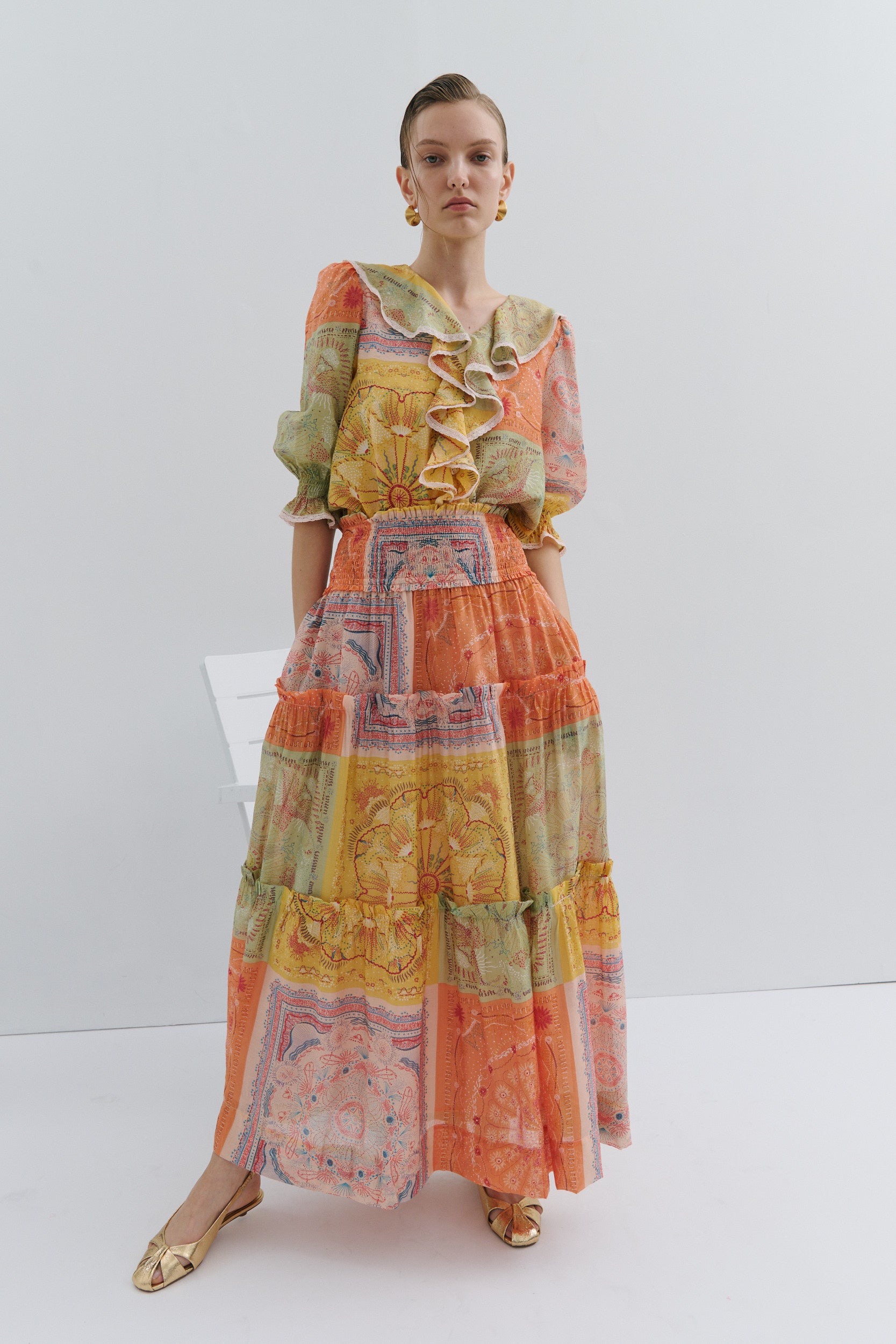 Model wearing a colorful patterned blouse and maxi skirt on a white background