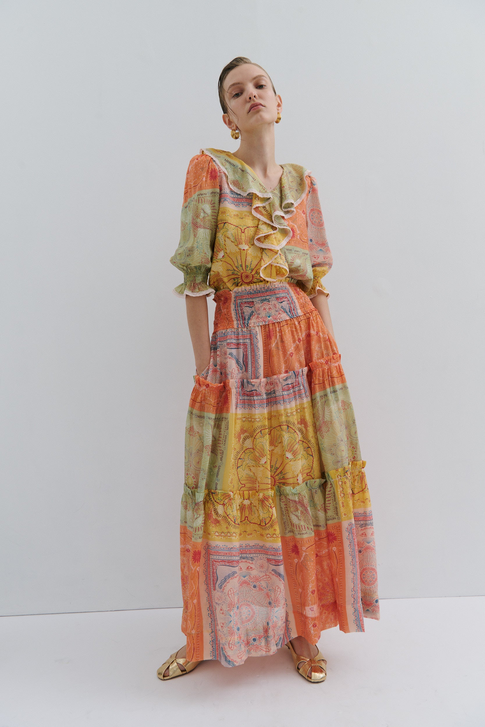 Woman wearing a colorful patterned boho frill shirt and nina maxi skirt by fashion brand Maevarii, on a white background