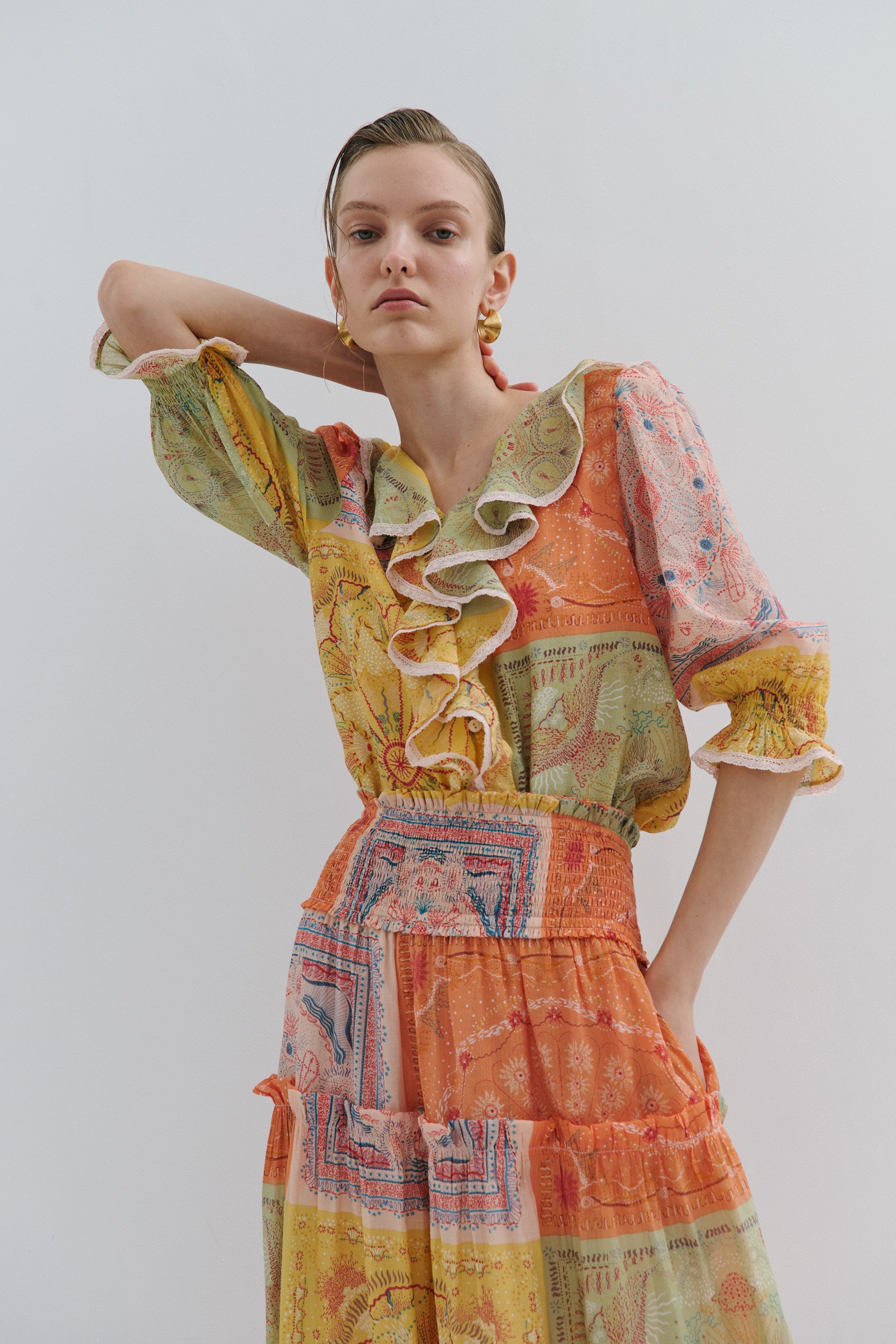 Woman wearing a colorful patchwork boho frill shirt against a plain background
