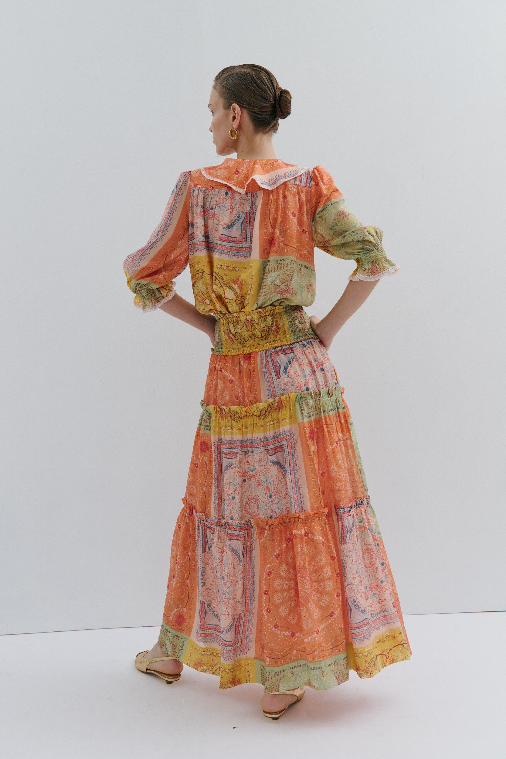 Woman wearing a colorful patchwork top and skirt against a white background