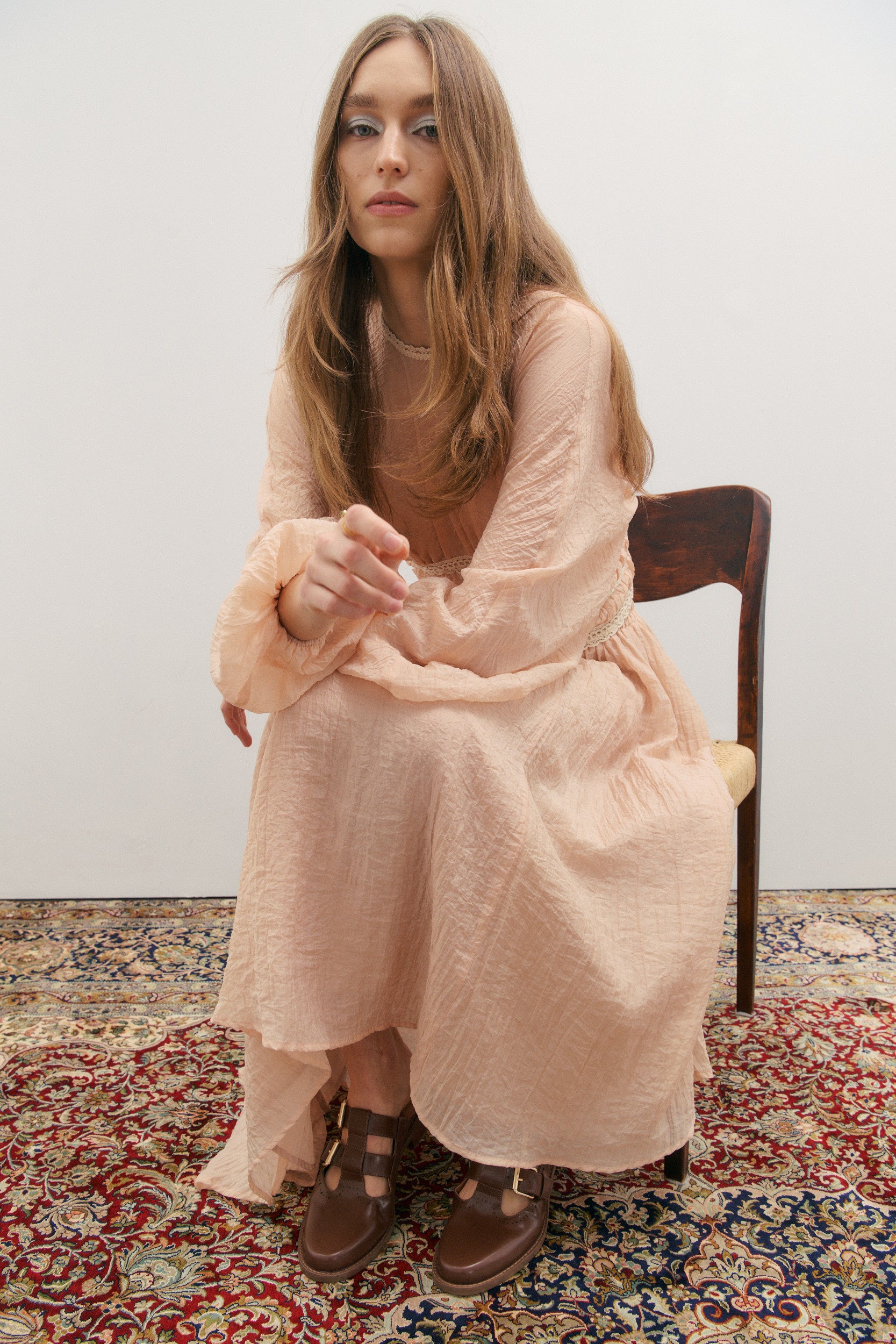 Woman in a pink outfit sitting on a wooden chair on a patterned rug.