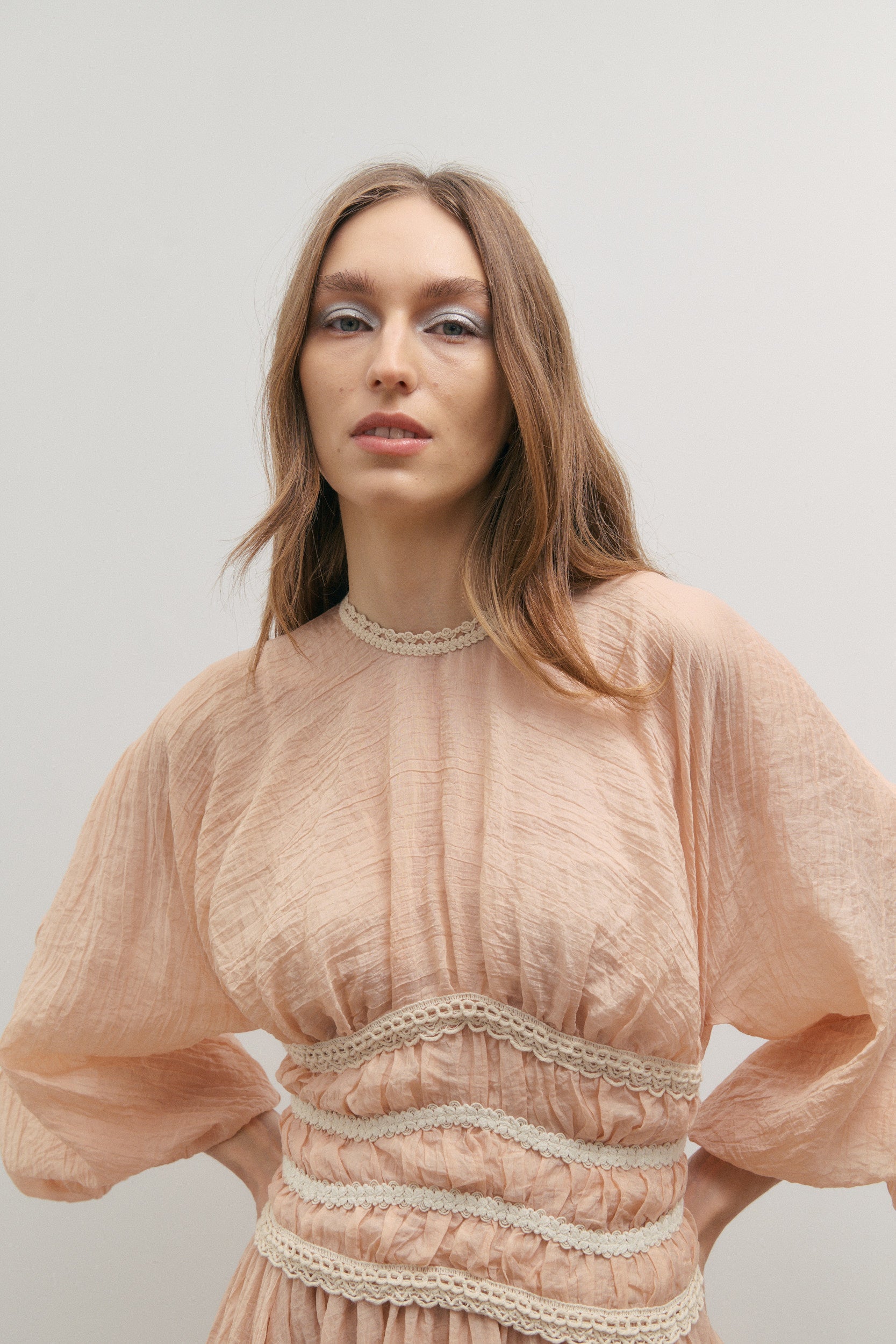 Woman wearing a light pink top with lace details against a plain background