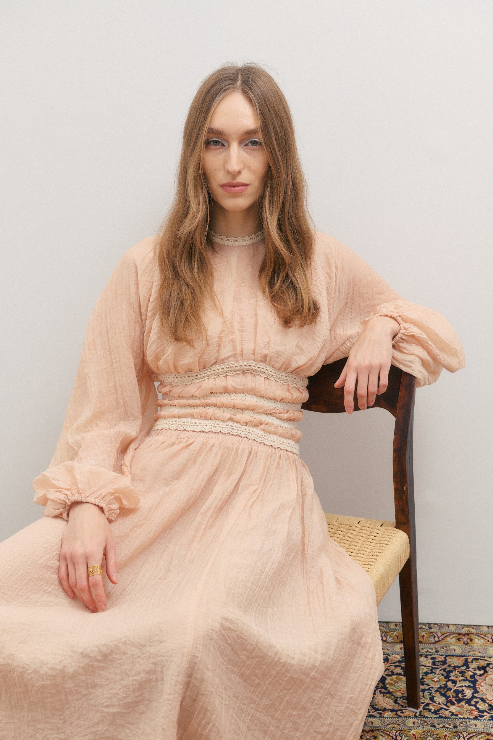 Woman in a light pink designer outfit by Maevarii, sitting on a chair against a plain background