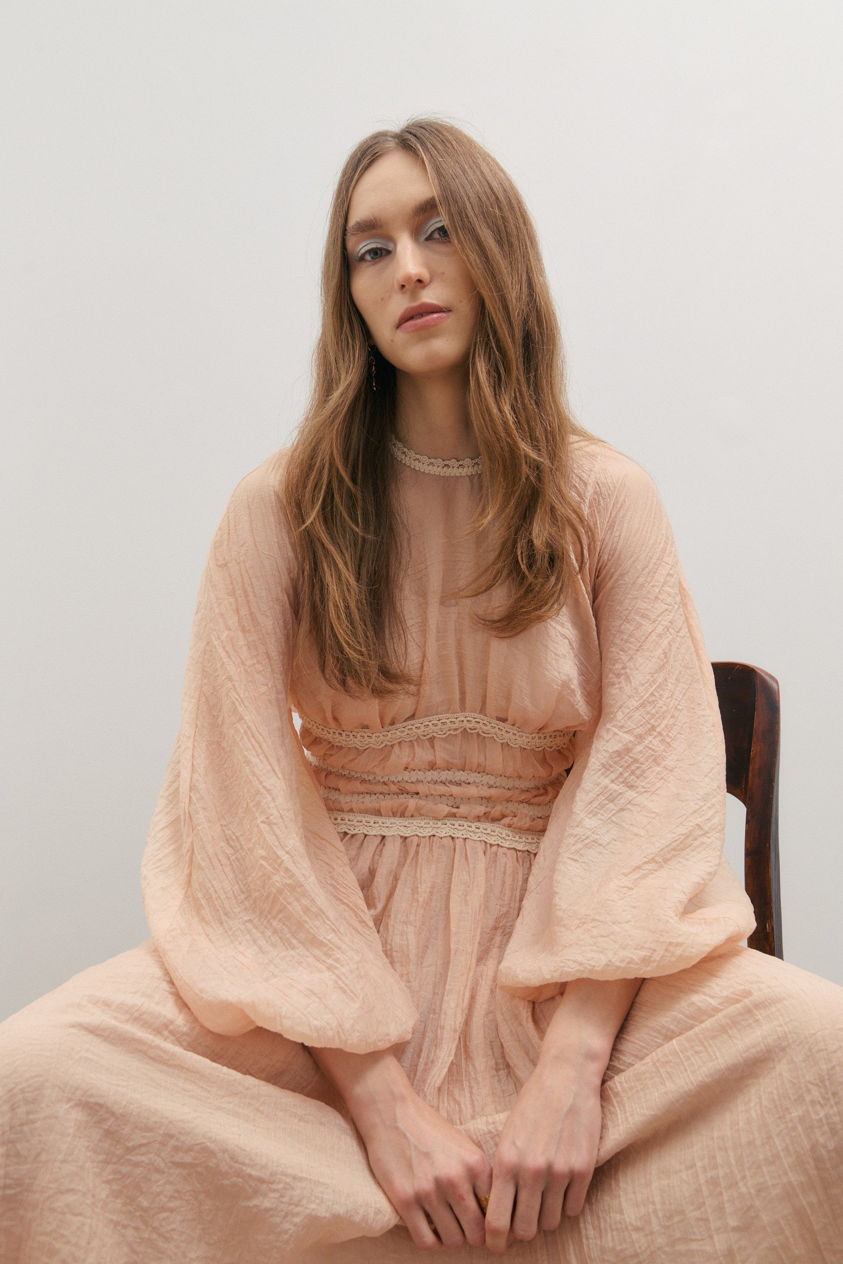 Woman wearing a peach-colored top and skirt sitting on a chair against a plain background