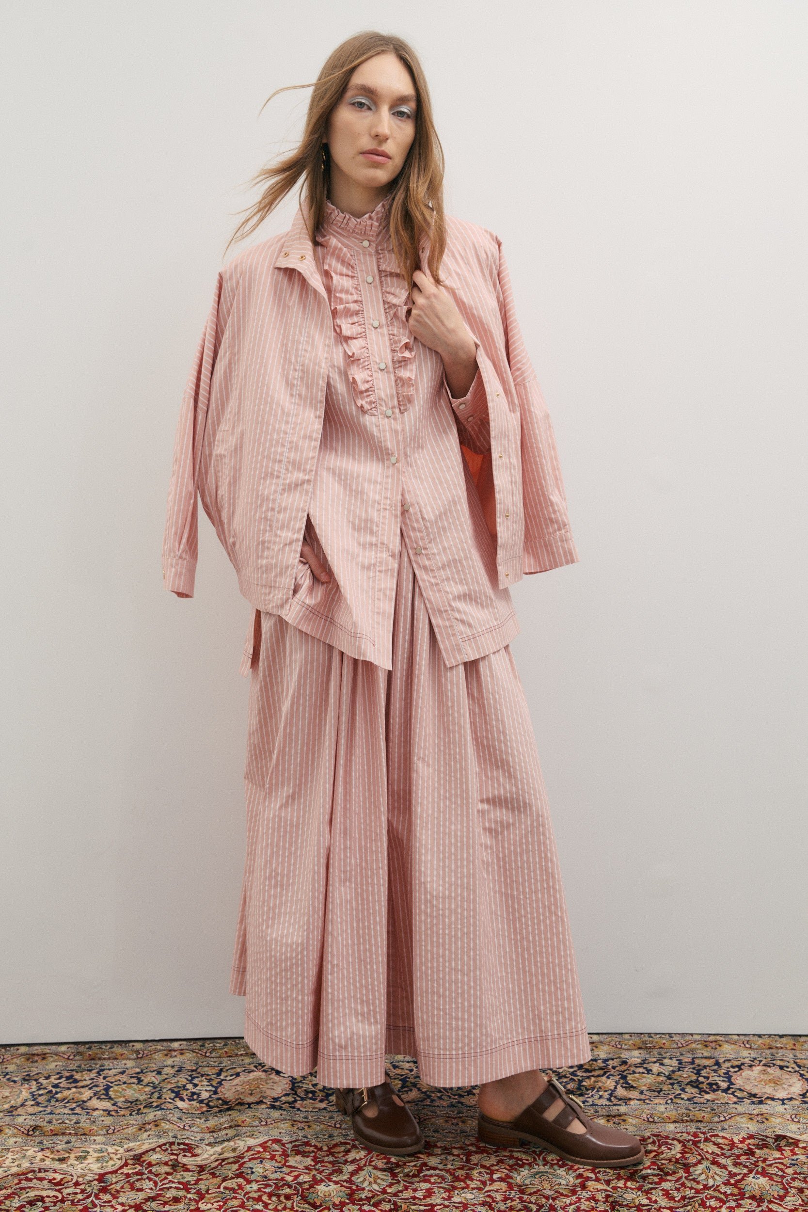 Woman wearing a pink outfit with a matching jacket and skirt on a plain background