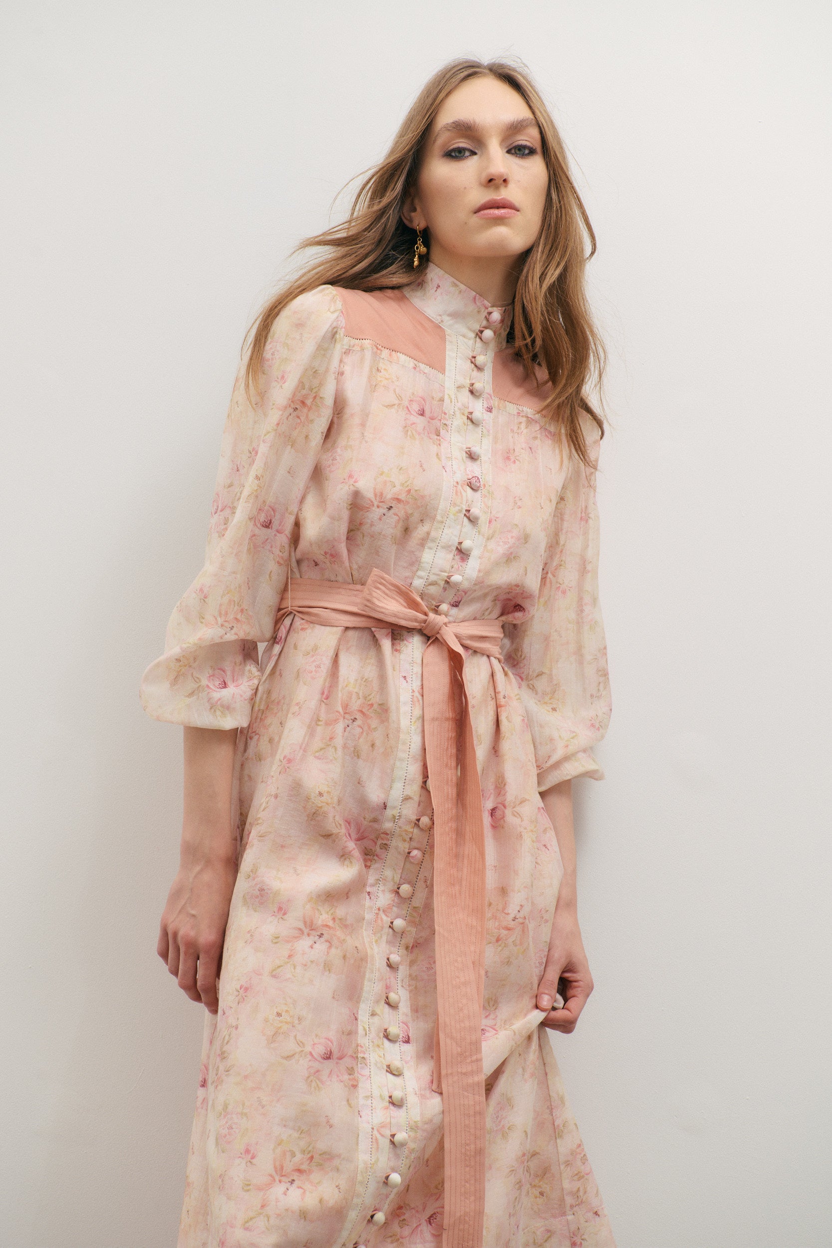 Woman wearing a floral dress with a pink belt against a white background