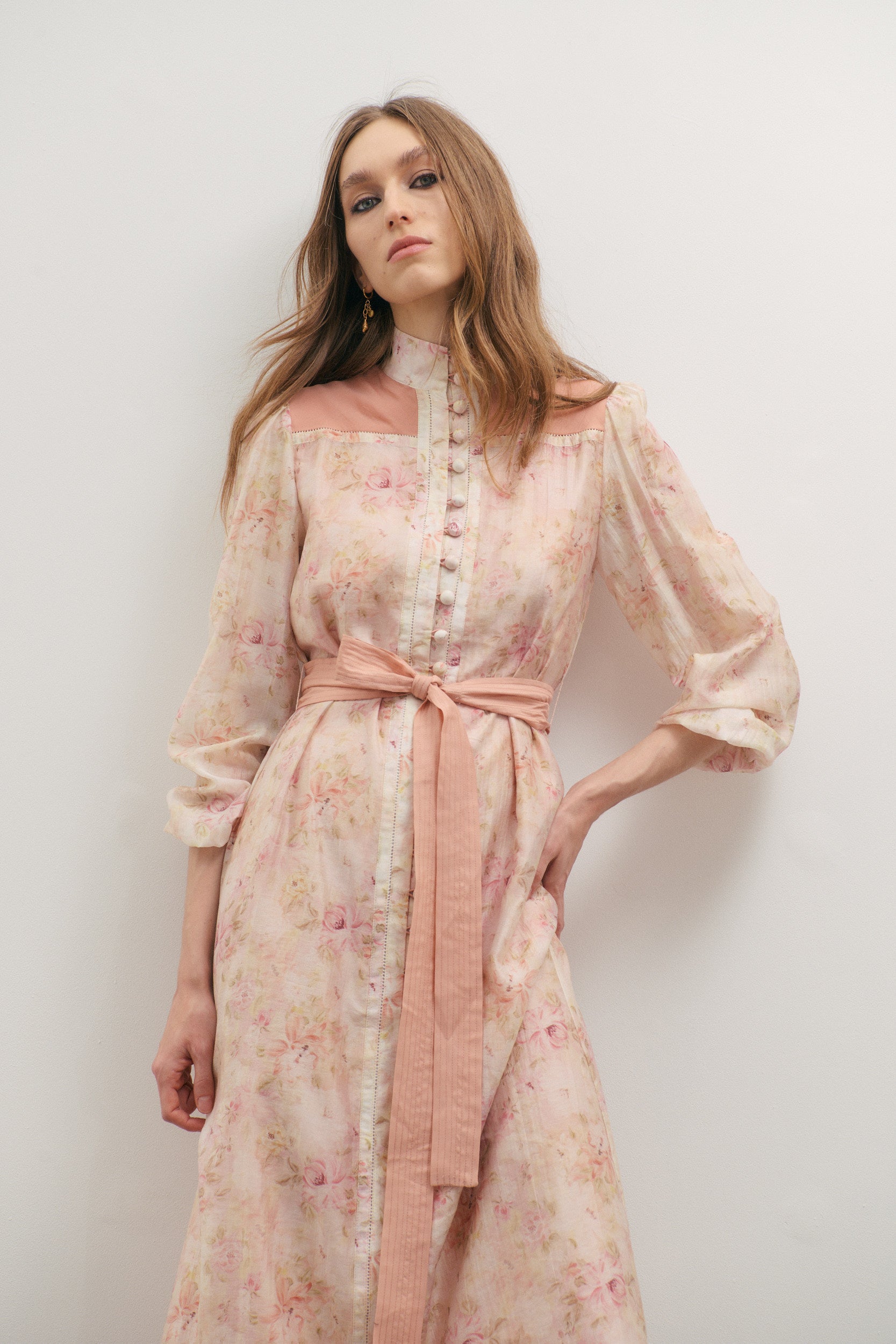 Woman wearing a floral dress with a pink belt against a white background