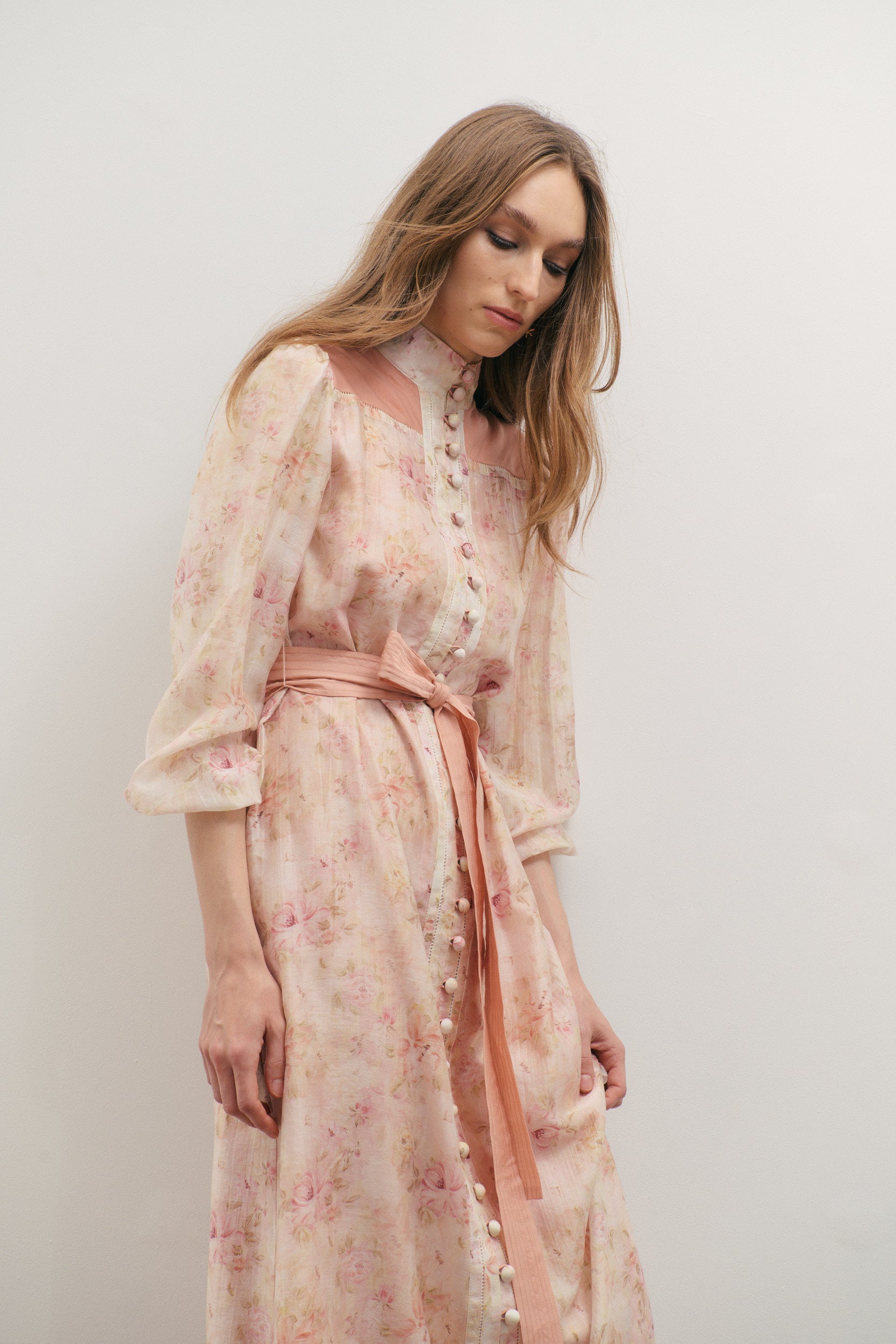 Woman wearing a floral dress with a belt against a plain background